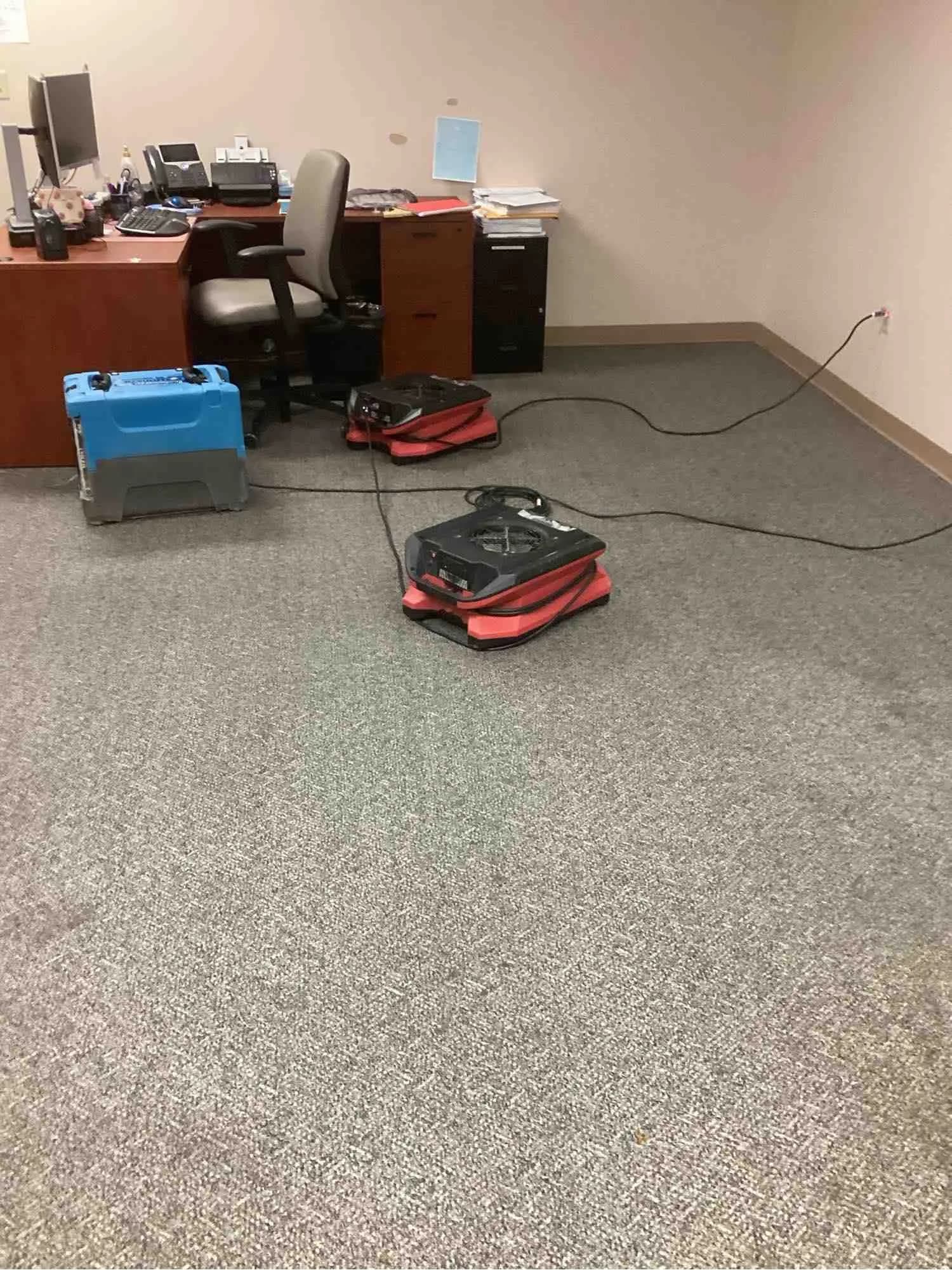 Two air movers running on damp office carpet with cables trailing back to the wall