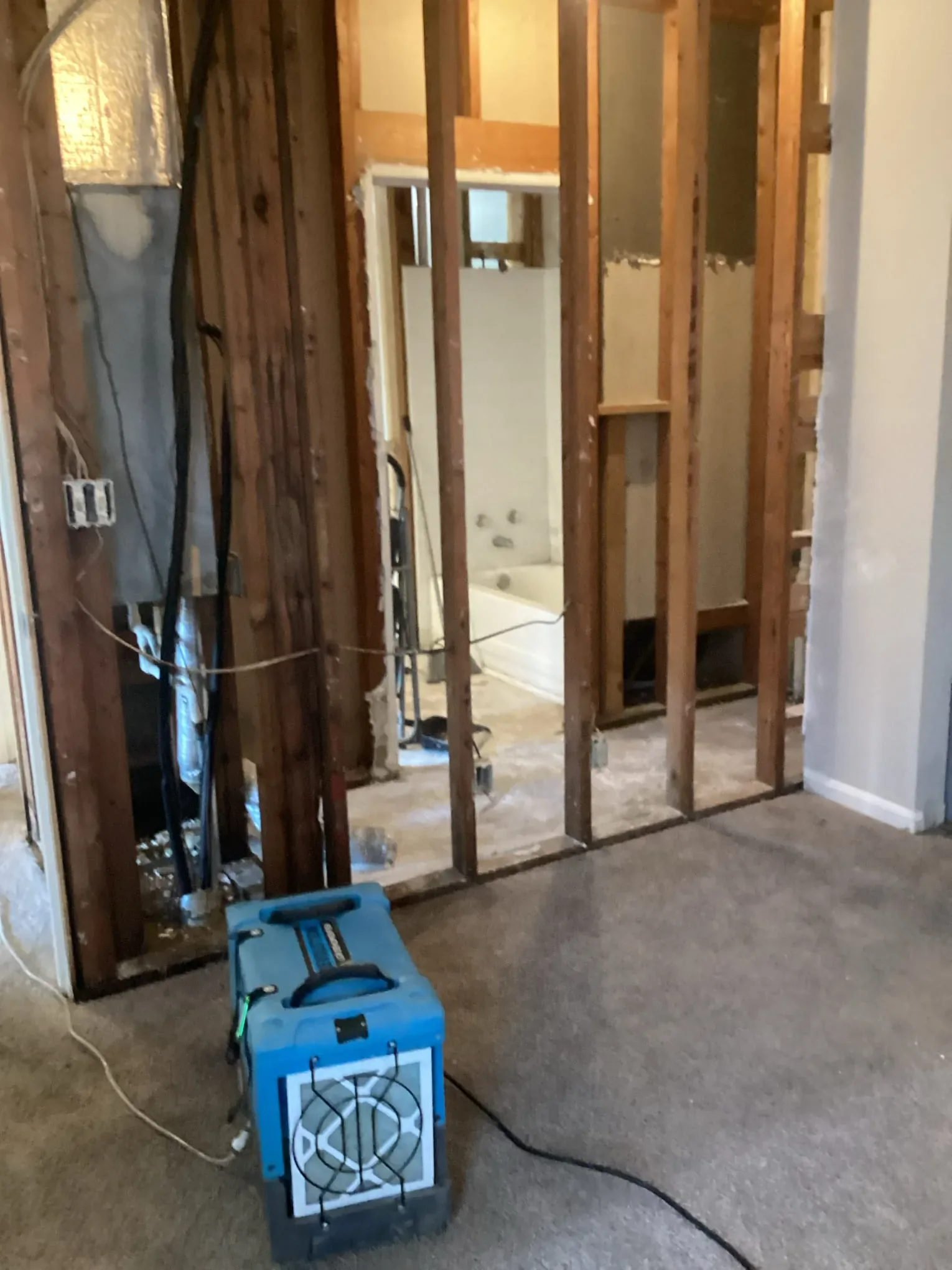 An air scrubber running on the floor beside a wall opened back to the studs, filtering the air in the work area