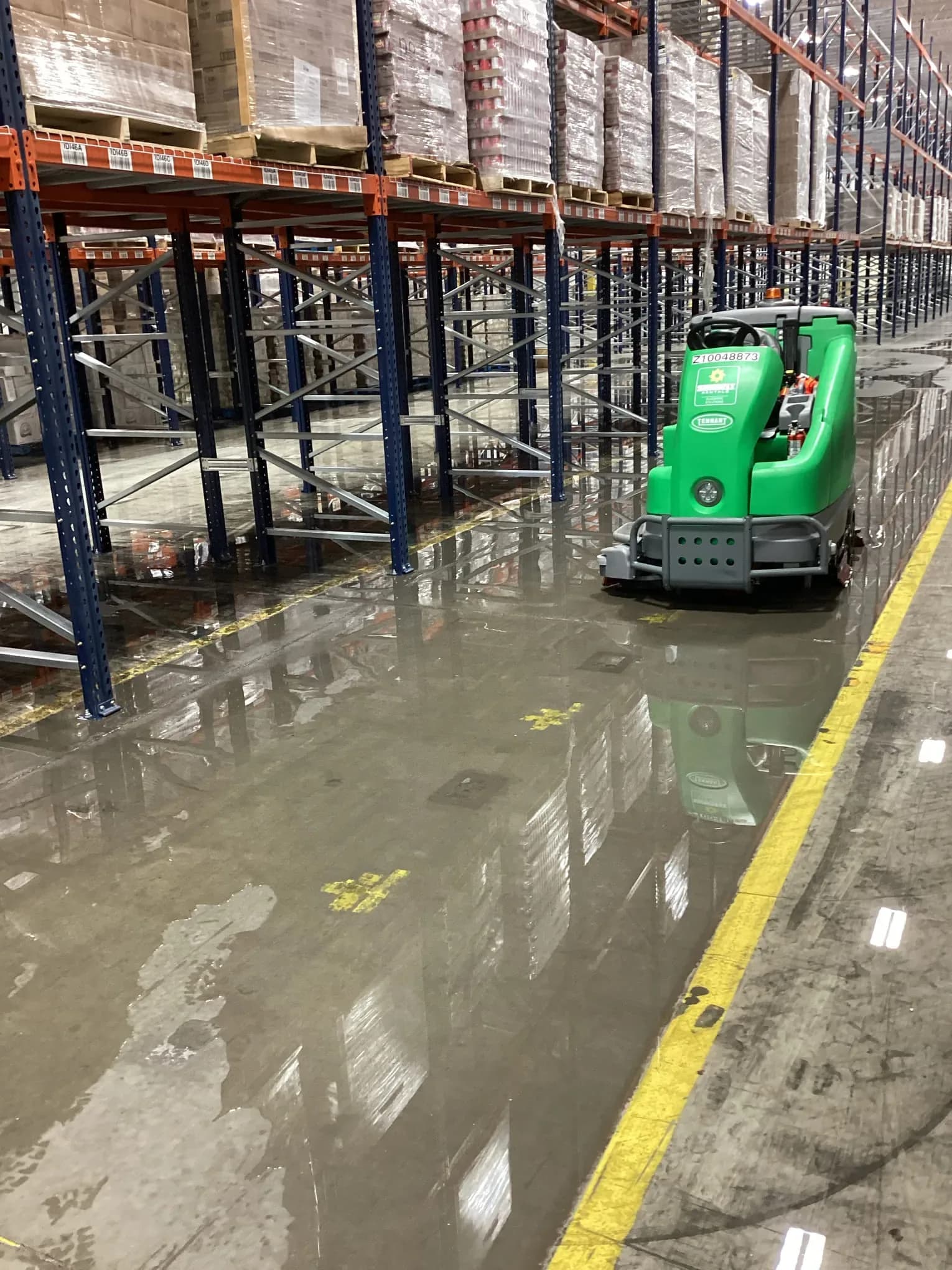 Technician running a floor scrubber to extract water across a warehouse floor