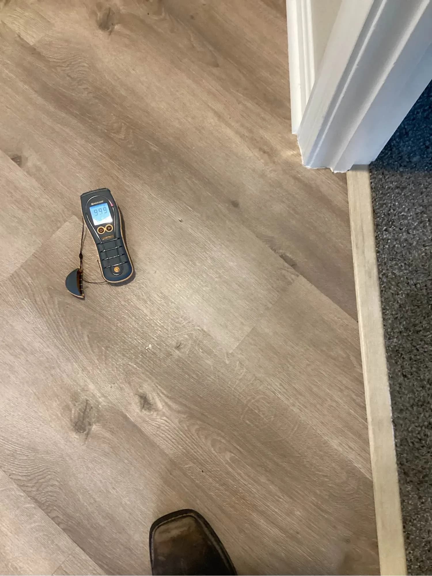 Moisture meter on a tiled floor in a doorway, checking how far water has travelled