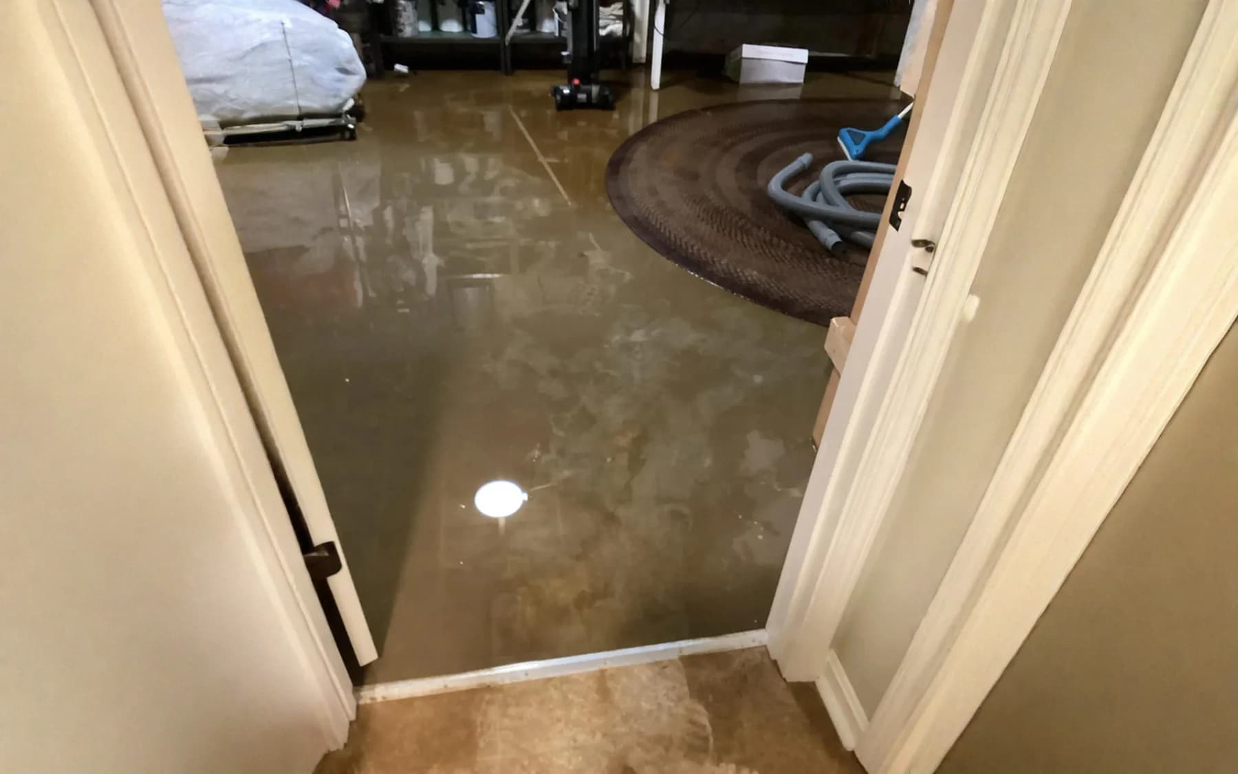 Murky brown standing water across a floor, seen through an open doorway, with an extraction hose run into it