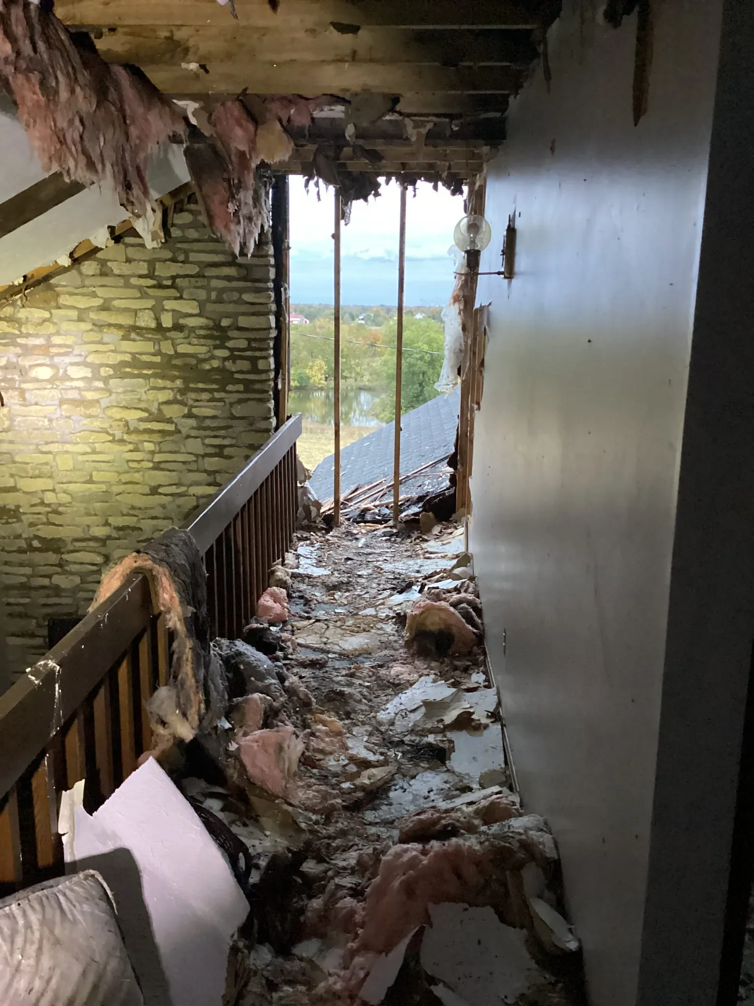 Interior hallway with the exterior wall torn open, insulation and debris across the floor and daylight coming through the gap