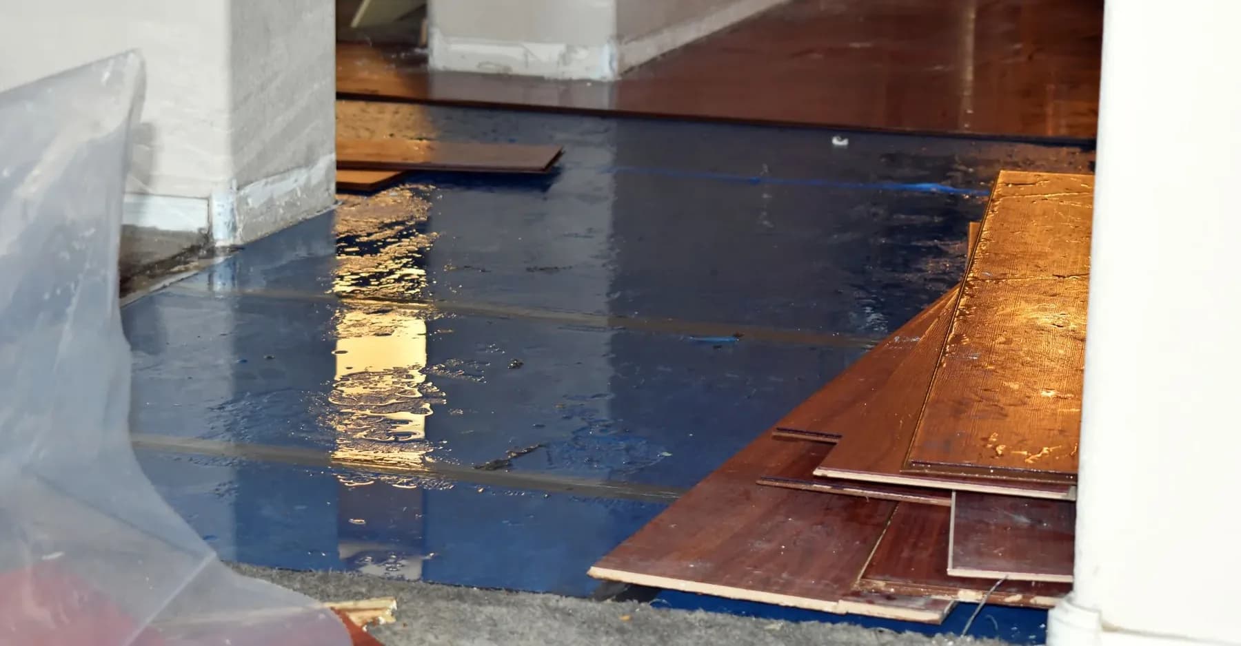 Water spread across hardwood flooring with plastic sheeting laid to one side